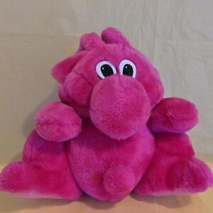 Peut inclure: Une peluche magenta avec de grands yeux ronds et un museau proéminent. Le jouet a une texture douce et floue et présente des oreilles et des membres arrondis. Le design est fantaisiste et adapté aux enfants.