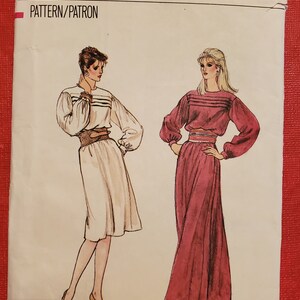 May include: Vogue Patterns sewing pattern featuring illustrations of two dresses. The pattern includes the size 12 and the number 8451. The dresses have long sleeves and are cinched at the waist. The dress on the left is white, and the dress on the right is burgundy.