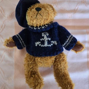 May include: A brown teddy bear wearing a blue knitted sweater with a white anchor design and a navy blue beret.