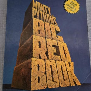 May include: The cover of "Monty Python's Big Red Book" features the title in large, textured, orange letters stacked like a pyramid against a dark blue background. A yellow starburst sticker reads "Special New Hardback Edition."