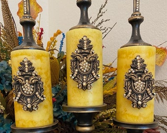 May include: A black metal candelabra with three candle holders. Each candle holder has a yellow candle with a gold and rhinestone design. The candelabra is decorated with rhinestones.