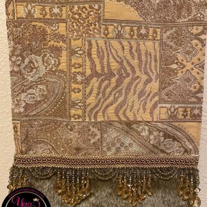 Pode incluir: Uma tape&ccedil;aria marrom e dourada com um padr&atilde;o paisley e uma borda de franja. A franja &eacute; feita de contas douradas e tem um suporte de pele marrom. A tape&ccedil;aria tem um design de patchwork com diferentes padr&otilde;es e texturas. A parte inferior da tape&ccedil;aria tem uma borda vermelha e dourada com um design de corrente.