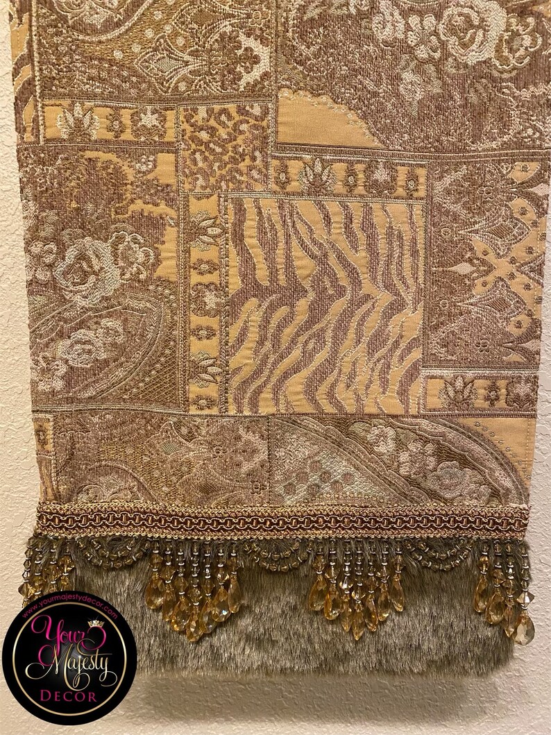 Pode incluir: Uma tape&ccedil;aria marrom e dourada com um padr&atilde;o paisley e uma borda de franja. A franja &eacute; feita de contas douradas e tem um suporte de pele marrom. A tape&ccedil;aria tem um design de patchwork com diferentes padr&otilde;es e texturas. A parte inferior da tape&ccedil;aria tem uma borda vermelha e dourada com um design de corrente.