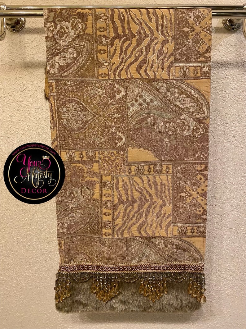 Pode incluir: Um corredor de mesa marrom e bege com um design de paisley e zebra. O corredor tem uma franja de contas com uma guarni&ccedil;&atilde;o de pele sint&eacute;tica. O texto "Your Majesty Decor" &eacute; vis&iacute;vel no canto inferior esquerdo da imagem.