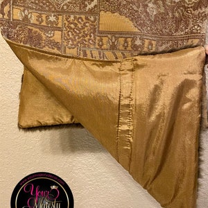 Pode incluir: Um tecido estampado em marrom e dourado com forro de cetim dourado. O tecido tem um design paisley e est&aacute; dobrado ao meio. O tecido &eacute; etiquetado com o texto "Your Majesty Decor" e o endere&ccedil;o do site "www.yourmajestydecor.com".