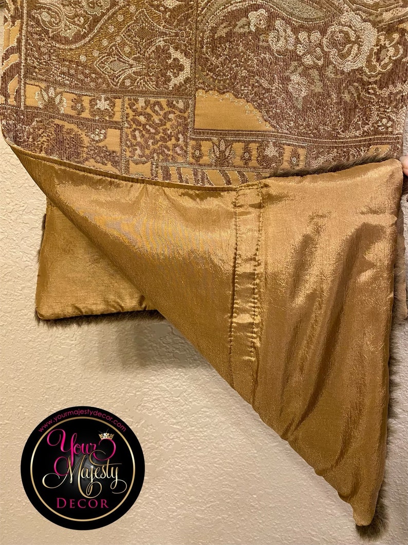 Pode incluir: Um tecido estampado em marrom e dourado com forro de cetim dourado. O tecido tem um design paisley e est&aacute; dobrado ao meio. O tecido &eacute; etiquetado com o texto "Your Majesty Decor" e o endere&ccedil;o do site "www.yourmajestydecor.com".