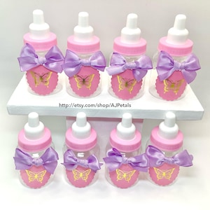 Puede incluir: Ocho biberones de pl&aacute;stico transparente con tetinas blancas y tapas rosas. Cada botella tiene una etiqueta rosa festoneada con una mariposa dorada y un lazo de sat&eacute;n color lavanda. El texto dice http://etsy.com/shop/AJPetals.