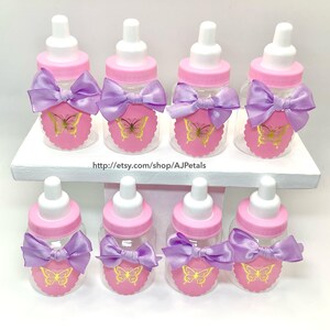 Puede incluir: Ocho biberones de pl&aacute;stico transparente con tetinas blancas y tapas rosas. Cada botella tiene una etiqueta rosa festoneada con una mariposa dorada y un lazo de sat&eacute;n color lavanda. El texto dice http://etsy.com/shop/AJPetals.