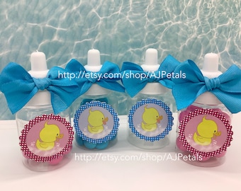 May include: Four clear plastic baby bottles with blue and pink polka dot labels featuring a yellow rubber duck. Each bottle is decorated with a blue ribbon bow and filled with small blue and pink candy.