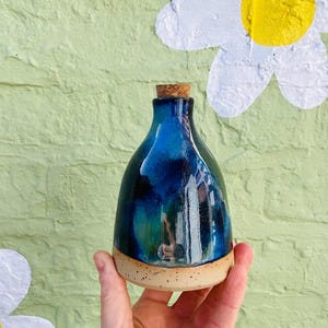 Peut inclure: Une bouteille en c&eacute;ramique faite &agrave; la main avec un bouchon en li&egrave;ge. La bouteille a un vernis bleu fonc&eacute; brillant avec des accents turquoise et noirs. La base est de couleur beige naturel non &eacute;maill&eacute;e. La bouteille est tenue dans une main.