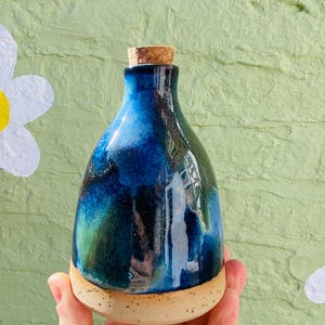 Peut inclure: Une bouteille en c&eacute;ramique faite &agrave; la main avec un bouchon en li&egrave;ge. La bouteille pr&eacute;sente un gla&ccedil;age bleu fonc&eacute; brillant avec des accents verts et noirs. La base est de couleur beige naturel non &eacute;maill&eacute;e.