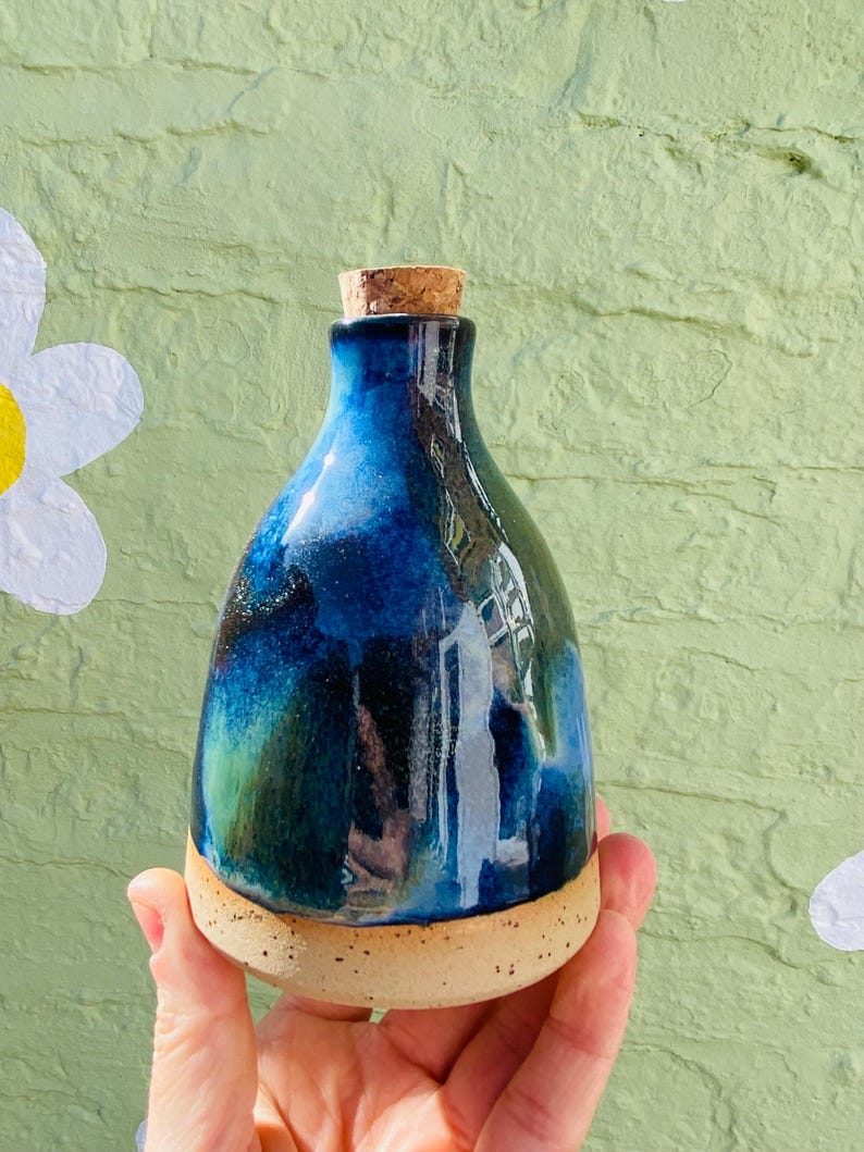 Peut inclure: Une bouteille en c&eacute;ramique faite &agrave; la main avec un bouchon en li&egrave;ge. La bouteille pr&eacute;sente un gla&ccedil;age bleu fonc&eacute; brillant avec des accents verts et noirs. La base est de couleur beige naturel non &eacute;maill&eacute;e.
