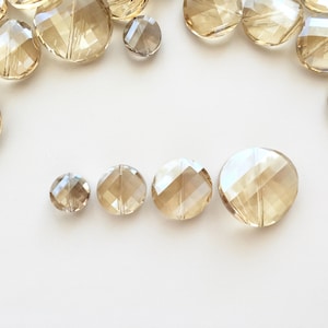 May include: Assortment of clear glass beads with a faceted design. The beads are various sizes and are arranged in a semi-circle on a white background.