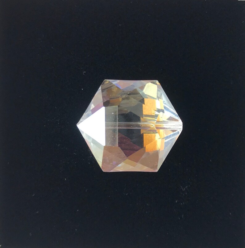 May include: A clear glass crystal bead with a faceted design. The bead has a hexagonal shape and is iridescent.