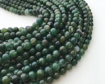 May include: A strand of dark green agate beads, each bead is round and smooth. The beads are arranged in a circular pattern, creating a visually appealing display.