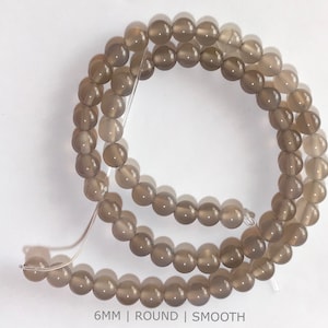 May include: A strand of smooth, round, grey agate beads. The beads are 6 mm in diameter.