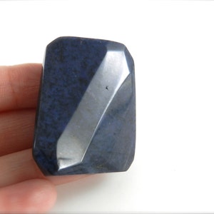 May include: A dark blue, faceted, rectangular stone with a rough, textured surface.