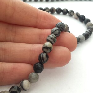 May include: A strand of black and white striped gemstone beads. The beads are round and have a smooth, polished finish.
