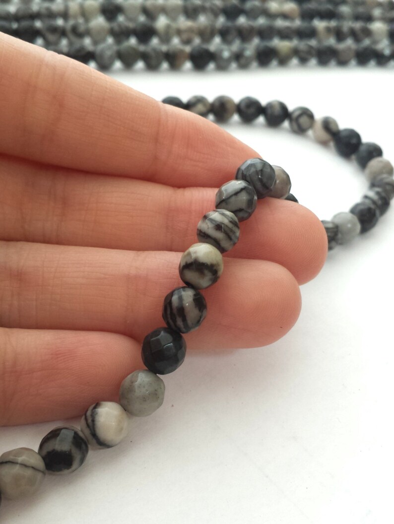 May include: A strand of black and white striped gemstone beads. The beads are round and have a smooth, polished finish.