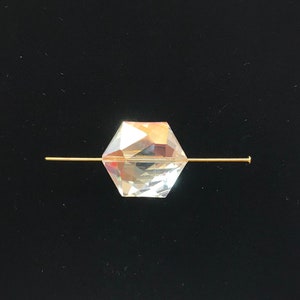 May include: A clear crystal bead with a faceted design is threaded onto a gold wire.