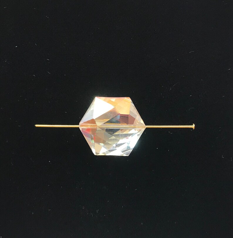 May include: A clear crystal bead with a faceted design is threaded onto a gold wire.