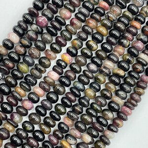 May include: A strand of black tourmaline beads with green, pink, and gold inclusions. The beads are oval shaped and have a smooth, polished finish.