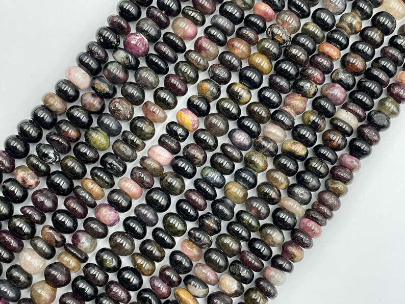 May include: A strand of black tourmaline beads with green, pink, and gold inclusions. The beads are oval shaped and have a smooth, polished finish.