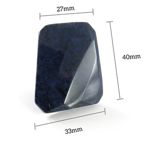 May include: A dark blue, faceted, gemstone with a rough, natural texture. It measures approximately 40mm tall, 27mm wide, and 33mm deep.