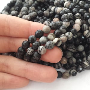 May include: A strand of black and white striped gemstone beads. The beads are faceted and have a natural, organic look.