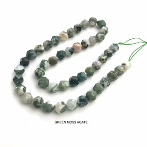May include: Strand of faceted green moss agate beads. The beads have a mix of green, white, and gray colors. The text "GREEN MOSS AGATE" is printed at the bottom of the image. The beads are strung on a green thread.