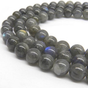 May include: A strand of gray labradorite gemstone beads. The beads are round and have a smooth, polished finish. The labradorite has a iridescent sheen, with flashes of blue, green, and gold.