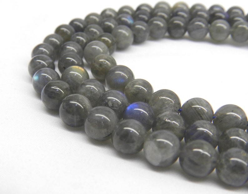 May include: A strand of gray labradorite gemstone beads. The beads are round and have a smooth, polished finish. The labradorite has a iridescent sheen, with flashes of blue, green, and gold.