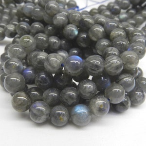 May include: A strand of round, gray labradorite beads with iridescent blue and green flashes. The beads are strung on a thin, blue thread.