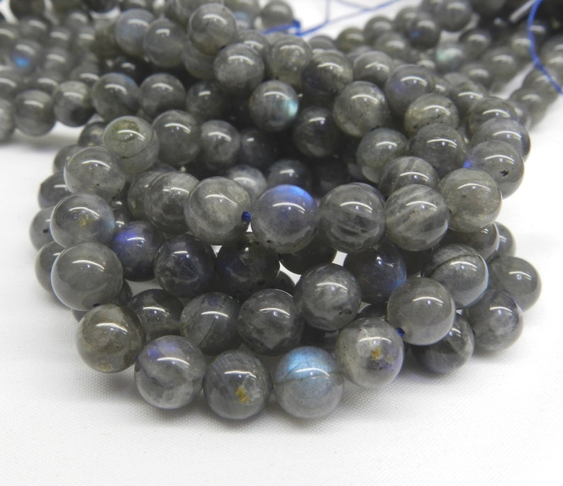 May include: A strand of round, gray labradorite beads with iridescent blue and green flashes. The beads are strung on a thin, blue thread.