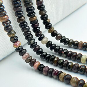 May include: A strand of black tourmaline beads with hints of pink, green, and brown. The beads are round and have a smooth, polished finish.