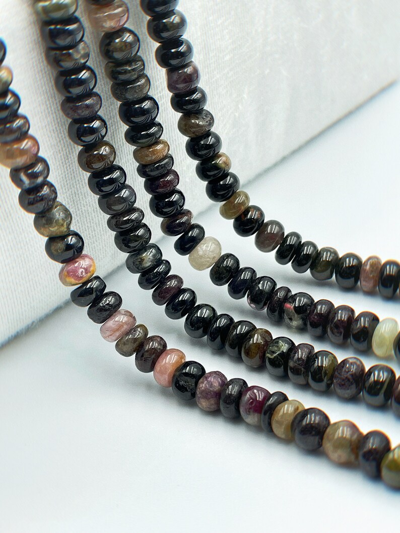 May include: A strand of black tourmaline beads with hints of pink, green, and brown. The beads are round and have a smooth, polished finish.