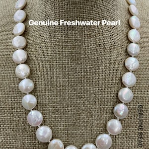 Puede incluir: Un collar de perlas de agua dulce blancas con perlas redondas. El collar se muestra en un maniquí de tela marrón.