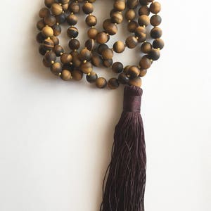 May include: A brown tiger's eye beaded mala necklace with a dark brown tassel.