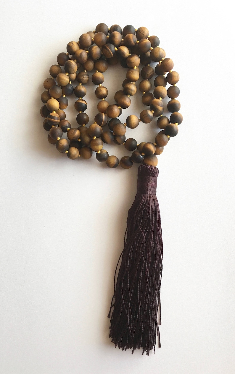 May include: A brown tiger's eye beaded mala necklace with a dark brown tassel.