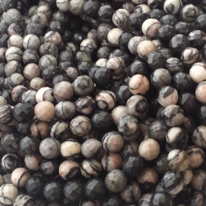 May include: A strand of black and white faceted gemstone beads. The beads are round and have a natural, organic look.