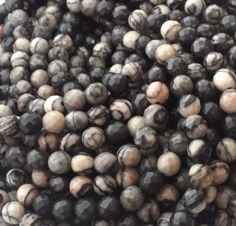 May include: A strand of black and white faceted gemstone beads. The beads are round and have a natural, organic look.