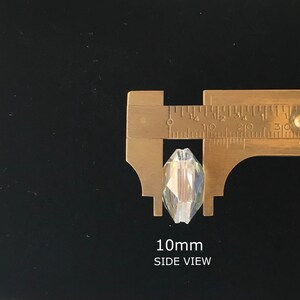 May include: A clear crystal bead with a faceted design, measured at 10mm in width. The bead is being measured with a caliper, showing the side view.