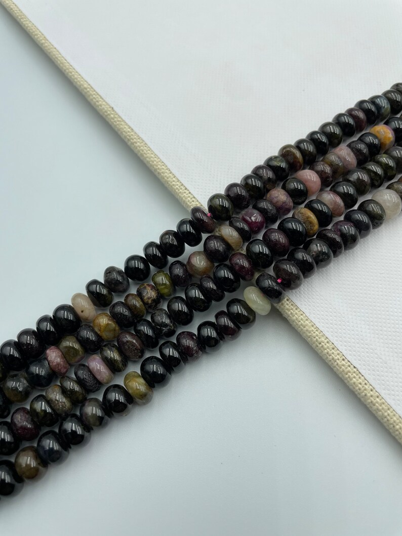 May include: A strand of black, green, and pink gemstone beads. The beads are round and have a smooth, polished finish.