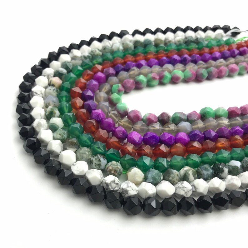 May include: A collection of faceted gemstone beads in various colors, including black, white, green, purple, and red. The beads are strung together, showcasing their geometric shapes and natural variations. Ideal for jewelry making or craft projects.
