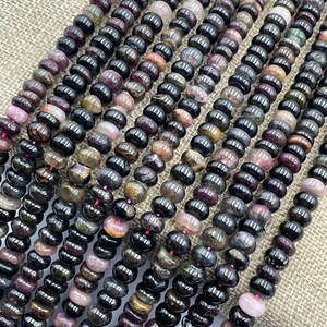 May include: A strand of black tourmaline beads with hints of pink, green, and brown. The beads are round and have a smooth, polished finish.