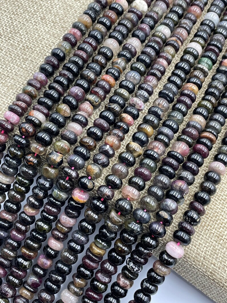 May include: A strand of black tourmaline beads with hints of pink, green, and brown. The beads are round and have a smooth, polished finish.