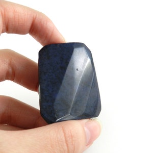 May include: A dark blue, faceted, polished stone with a smooth, slightly textured surface.
