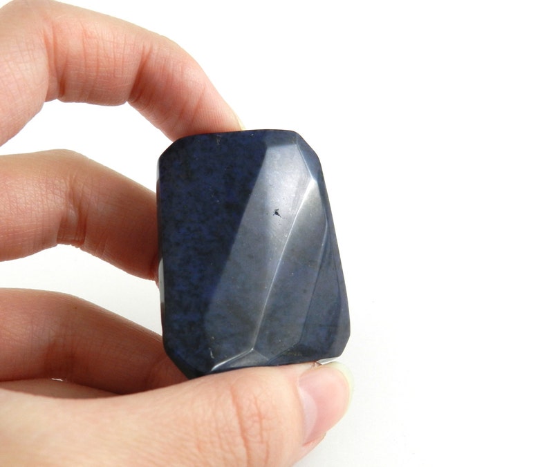 May include: A dark blue, faceted, polished stone with a smooth, slightly textured surface.