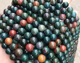 May include: A close-up of a pile of green, red, and brown gemstone beads. The beads are round and have a smooth, polished finish.