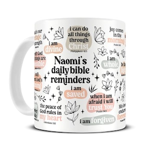 Peut inclure: Tasse en c&eacute;ramique blanche avec l'inscription "Naomi's daily bible reminders" et diverses phrases inspirantes et illustrations florales. La tasse comprend les phrases "I am saved", "I am forgiven" et "I can do all things through Christ".